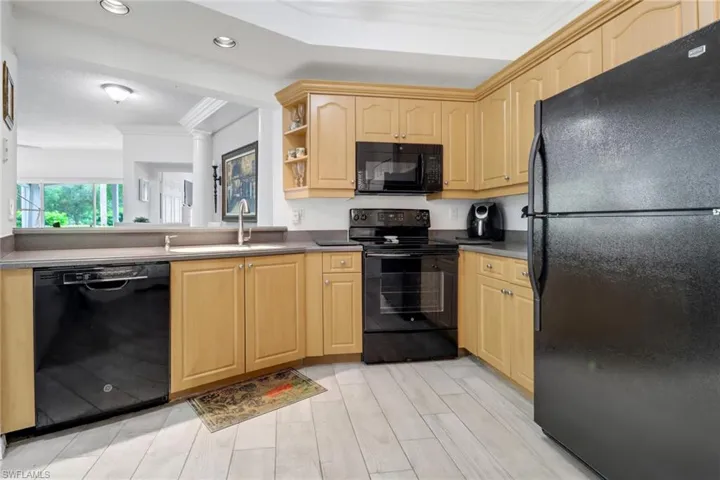 Kitchen featuring light brown cabinets, light hardwood / wood-style floors, black appliances, sink, and ornamental molding