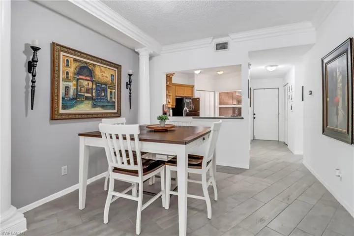 Dining area featuring a textured ceiling, decorative columns, and crown molding