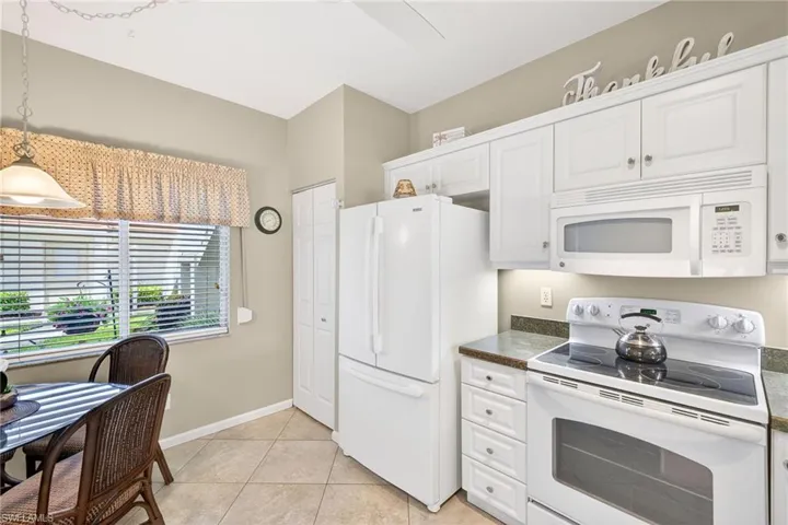 Kitchen featuring white appliances, dark countertops, white cabinetry, pendant lighting, and light tile patterned flooring