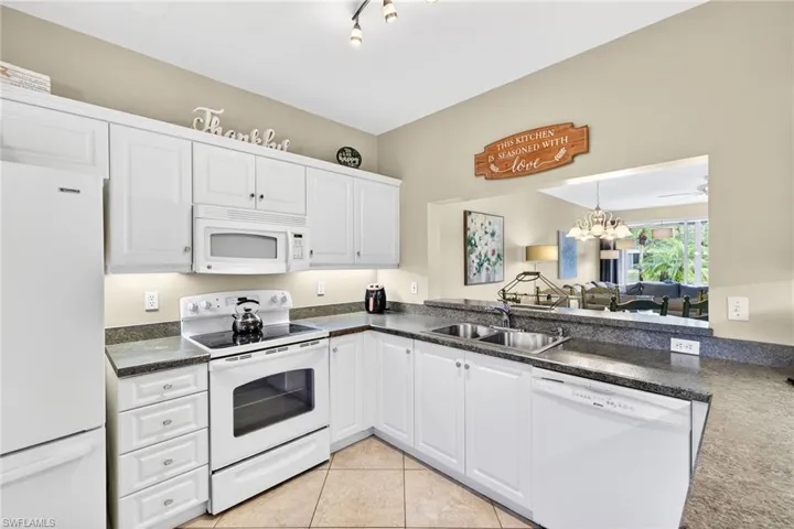 Kitchen featuring white appliances, white cabinets, decorative light fixtures, a chandelier, and light tile patterned floors