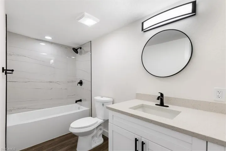 Full bathroom with toilet, vanity, tiled shower / bath, and wood-type flooring