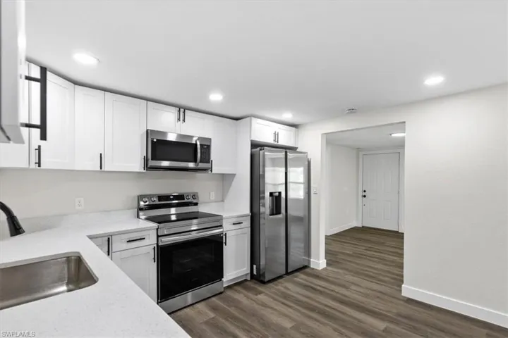 Kitchen with sink, stainless steel appliances, dark wood-type flooring, and white cabinets