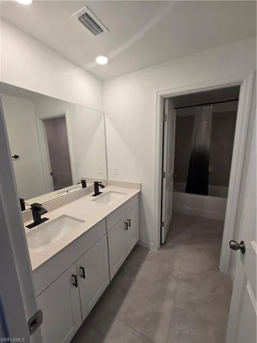 2nd Bathroom with double vanity, shower / bath combo, and tile patterned flooring