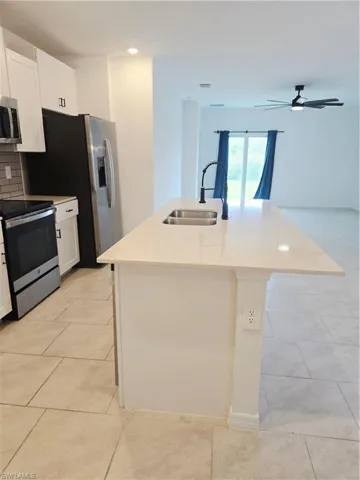 Kitchen featuring stove, light tile patterned floors, white cabinetry, a kitchen island with sink, and ceiling fan