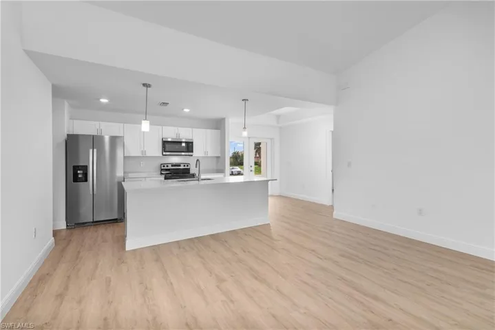 Kitchen with white cabinetry, light countertops, appliances with stainless steel finishes, an island with sink, and pendant lighting