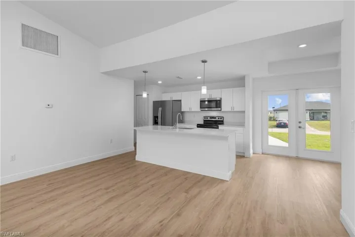 Kitchen featuring stainless steel appliances, visible vents, white cabinets, a sink, and an island with sink