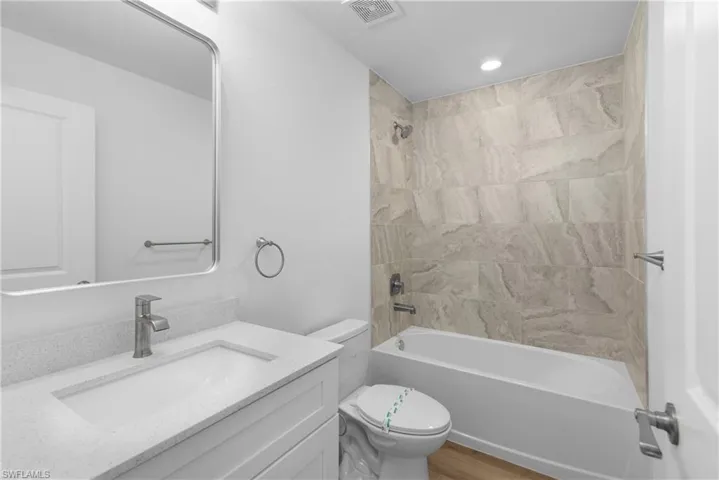 Bathroom featuring shower / tub combination, toilet, wood finished floors, vanity, and visible vents