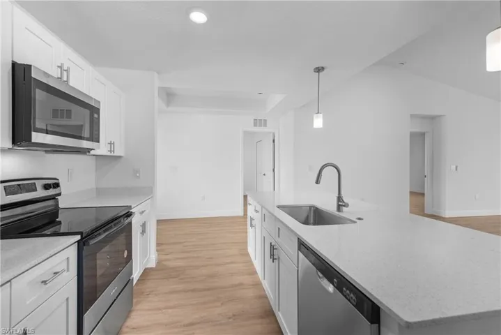 Kitchen with an island with sink, hanging light fixtures, stainless steel appliances, white cabinetry, and a sink
