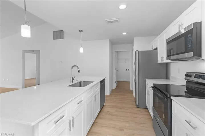 Kitchen with a center island with sink, white cabinets, decorative light fixtures, stainless steel appliances, and a sink