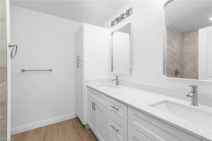 Full bath with double vanity, a sink, baseboards, and wood finished floors