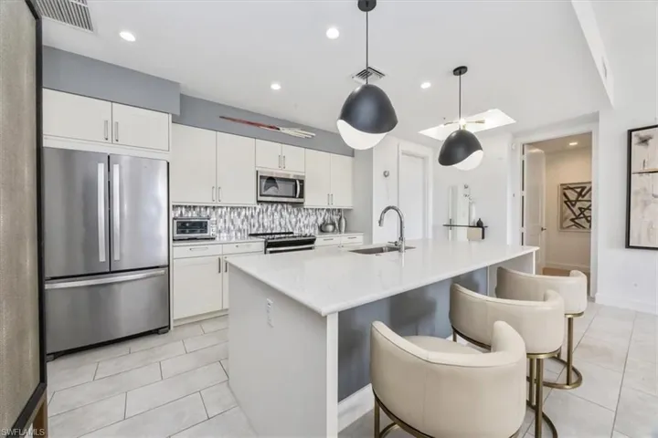 Kitchen with decorative light fixtures, stainless steel appliances, a kitchen breakfast bar, white cabinets, and recessed lighting