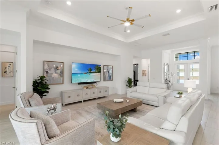 Living room with a raised ceiling, ornamental molding, a ceiling fan, recessed lighting, and light wood-style floors