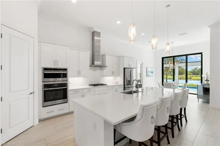Kitchen with crown molding, a breakfast bar, white cabinetry, a center island with sink, and pendant lighting