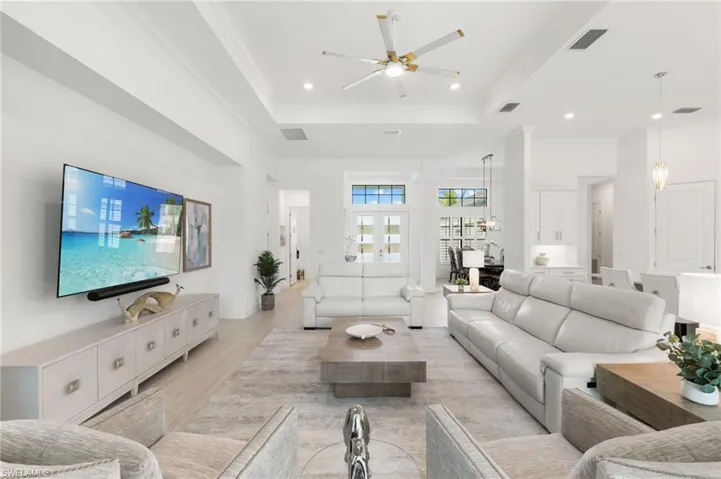 Living room featuring light wood finished floors, crown molding, a raised ceiling, recessed lighting, and a ceiling fan
