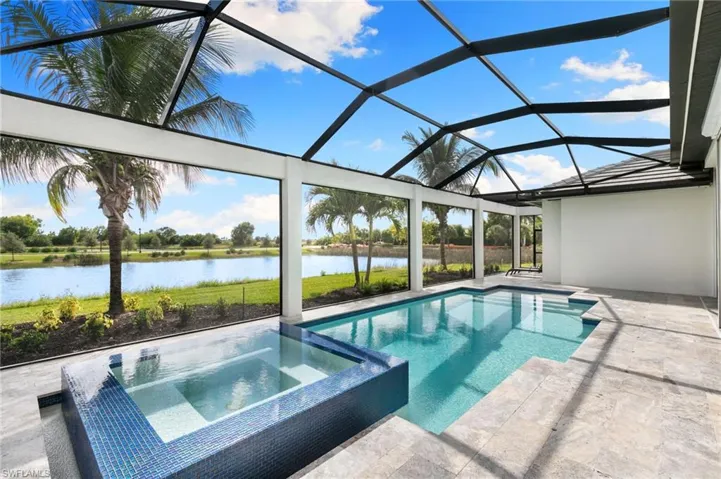 View of pool featuring a water view, a sunroom, a pool with connected hot tub, glass enclosure, and a patio