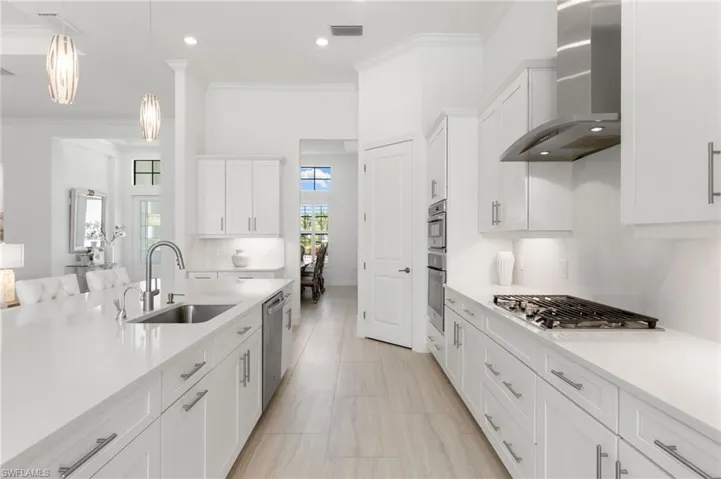 Kitchen featuring crown molding, white cabinetry, wall chimney exhaust hood, light stone countertops, and hanging light fixtures