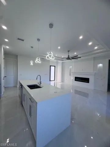 Kitchen with a large island with sink, a sink, a fireplace, marble finish floor, and visible vents
