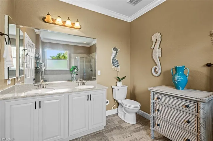 Bathroom with ornamental molding, a shower stall, toilet, double vanity, and baseboards