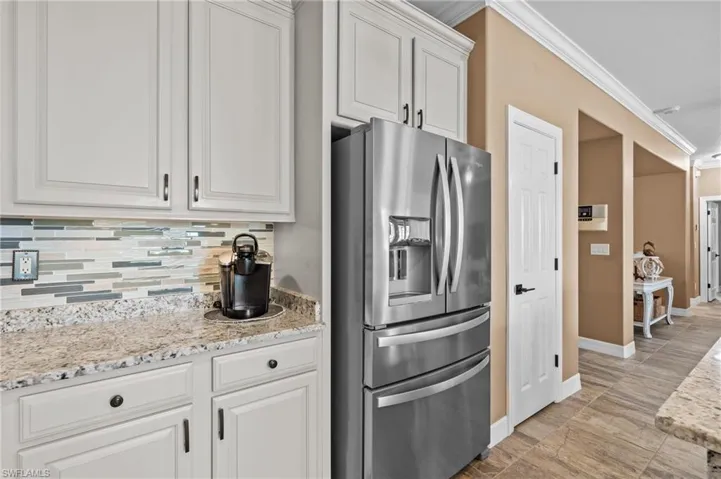 Kitchen featuring stainless steel fridge with ice dispenser, ornamental molding, tasteful backsplash, white cabinetry, and baseboards