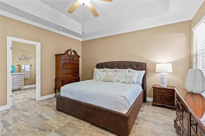 Bedroom featuring a tray ceiling, ornamental molding, ceiling fan, and baseboards