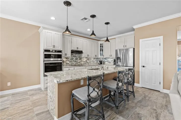 Kitchen with appliances with stainless steel finishes, a sink, under cabinet range hood, crown molding, and backsplash