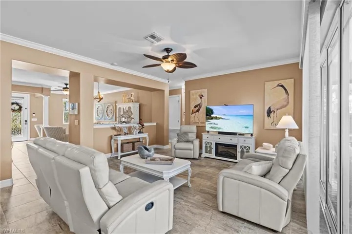 Living area featuring a ceiling fan, crown molding, light tile patterned floors, and baseboards