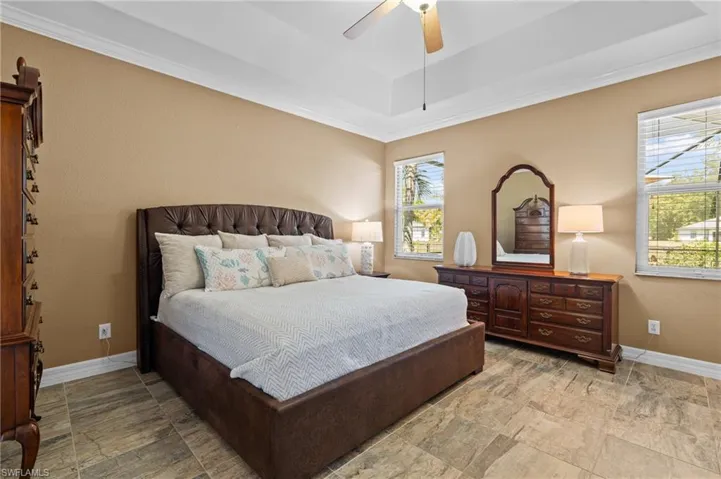 Bedroom featuring a tray ceiling, baseboards, a ceiling fan, and ornamental molding