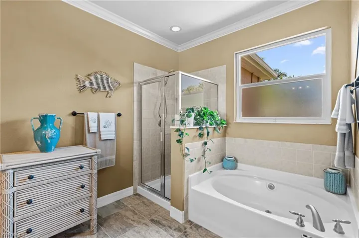 Bathroom featuring a stall shower, a garden tub, ornamental molding, and baseboards