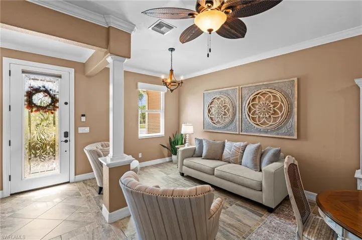 Living area with decorative columns, crown molding, baseboards, ceiling fan, and a chandelier