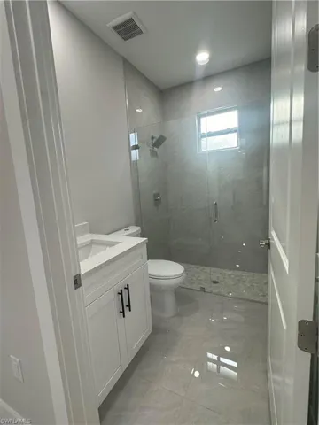Bathroom featuring a shower with shower door, vanity, toilet, and tile floors