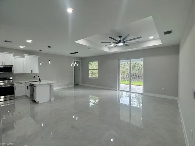 Kitchen featuring ceiling fan, a tray ceiling, light tile flooring, pendant lighting, and appliances with stainless steel finishes
