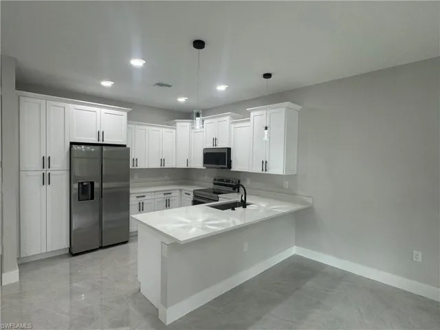 Kitchen featuring kitchen peninsula, stainless steel appliances, light tile flooring, pendant lighting, and white cabinets
