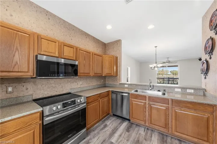 Kitchen with stainless steel appliances, a ceiling fan, light wood-style flooring, wood finish cabinets, and wallpapered walls