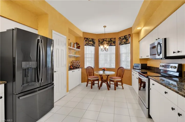 Kitchen with stainless steel appliances, dark stone countertops, white cabinets, decorative light fixtures, and a chandelier