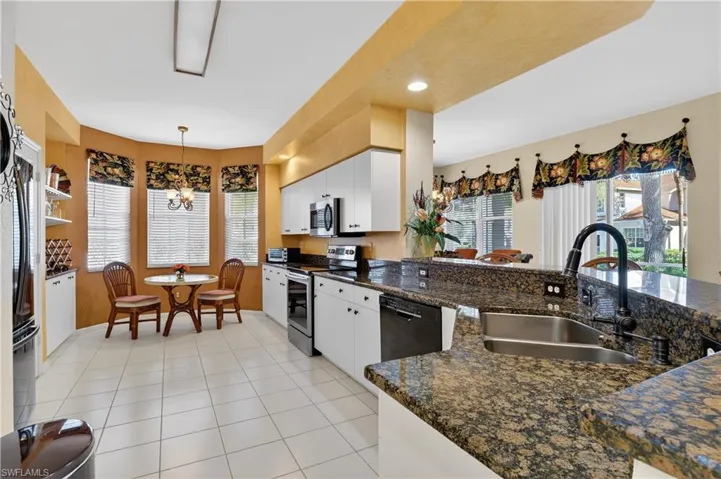 Kitchen with white cabinetry, stainless steel appliances, pendant lighting, light tile patterned floors, and a chandelier