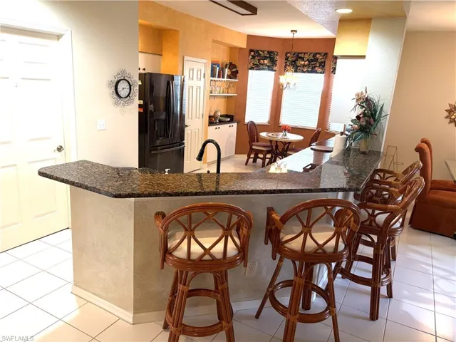 Kitchen featuring light tile patterned floors, black fridge with ice dispenser, a peninsula, a kitchen bar, and hanging light fixtures