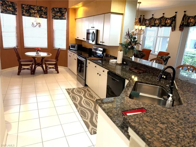 Kitchen with a chandelier, pendant lighting, appliances with stainless steel finishes, and dark stone counters