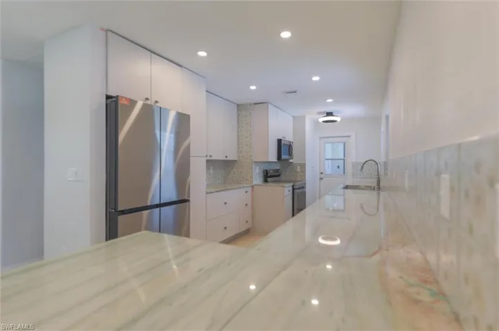 Kitchen with white cabinetry, tasteful backsplash, sink, light stone countertops, and appliances with stainless steel finishes