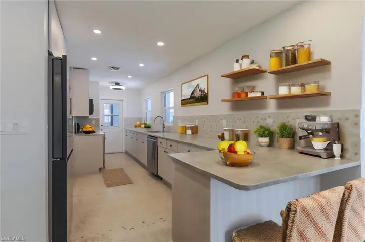 Kitchen featuring tasteful backsplash, kitchen peninsula, a kitchen bar, appliances with stainless steel finishes, and sink
