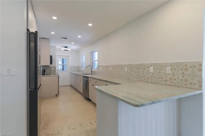Kitchen with appliances with stainless steel finishes, sink, kitchen peninsula, decorative backsplash, and light stone countertops