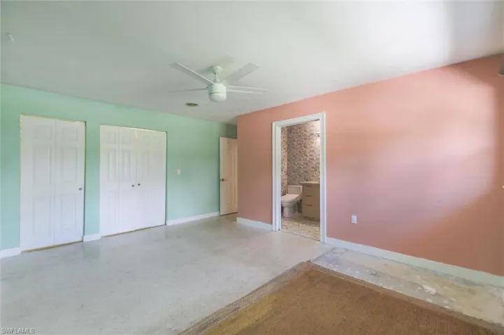Unfurnished bedroom featuring two closets, ensuite bath, and ceiling fan