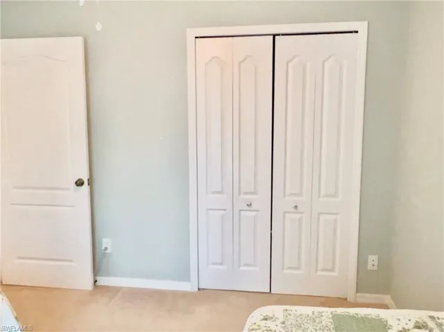 Twin bed guest bedroom featuring a closet, plantation shutters and light carpet