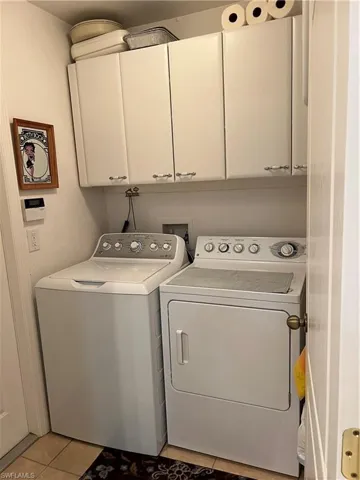 Laundry room with washer and clothes dryer, light tile patterned flooring, and cabinets