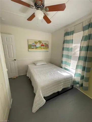 Room featuring a window with horizontal blinds, a white paneled door, and a ceiling fan with wood-finish blades