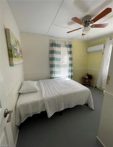 Interior space featuring painted wood flooring, a ceiling fan with integrated lighting, and a wall-mounted mini-split system