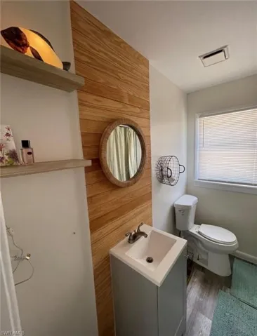 Bathroom featuring a wood-panel accent wall, a floating vanity with an integrated sink, a round mirror, and wood-finish flooring