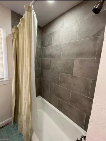 Bathtub featuring dark grey subway tile surround extending to the ceiling
