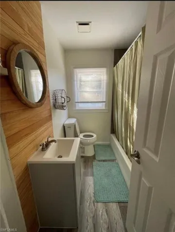 Bathroom featuring wood-finish accent wall, single vanity with integrated sink, wood-finish flooring, a window with blinds, and a built-in bathtub with shower