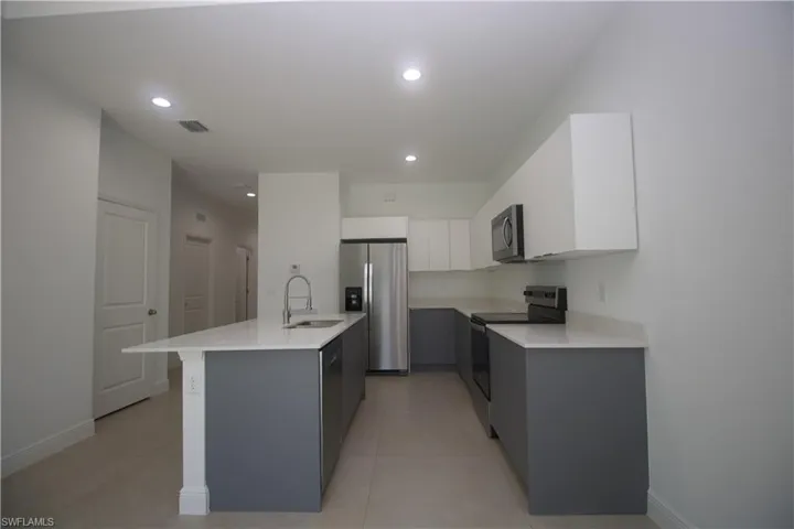 Kitchen featuring appliances with stainless steel finishes, gray cabinetry, a kitchen island with sink, sink, and white cabinets