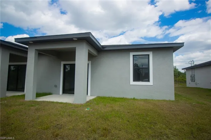 Rear view of house with a lawn, stucco siding, and a patio area